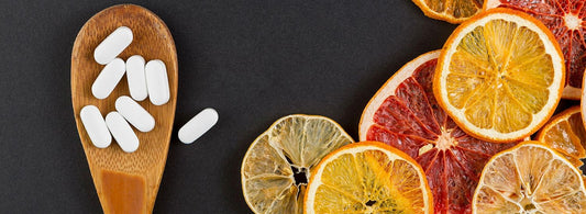 Verschiedene Obstsorten neben einem Holzlöffel mit Multivitamin-Tabletten, symbolisiert die sinnvolle Ergänzung von Nährstoffen in der Ernährung